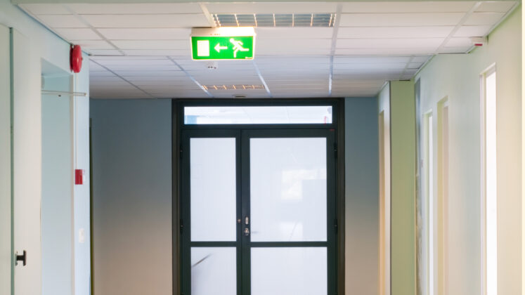 Illuminated emergency exit signage and lighting in a public building corridor.