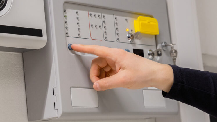 Fire Safety in Council Buildings: A Practical Guide for Facility Managers. Engineer testing a fire alarm control panel with status lights and system diagram visible.